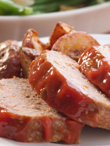 three slices of ketchup topped meatloaf with roasted potatoes.