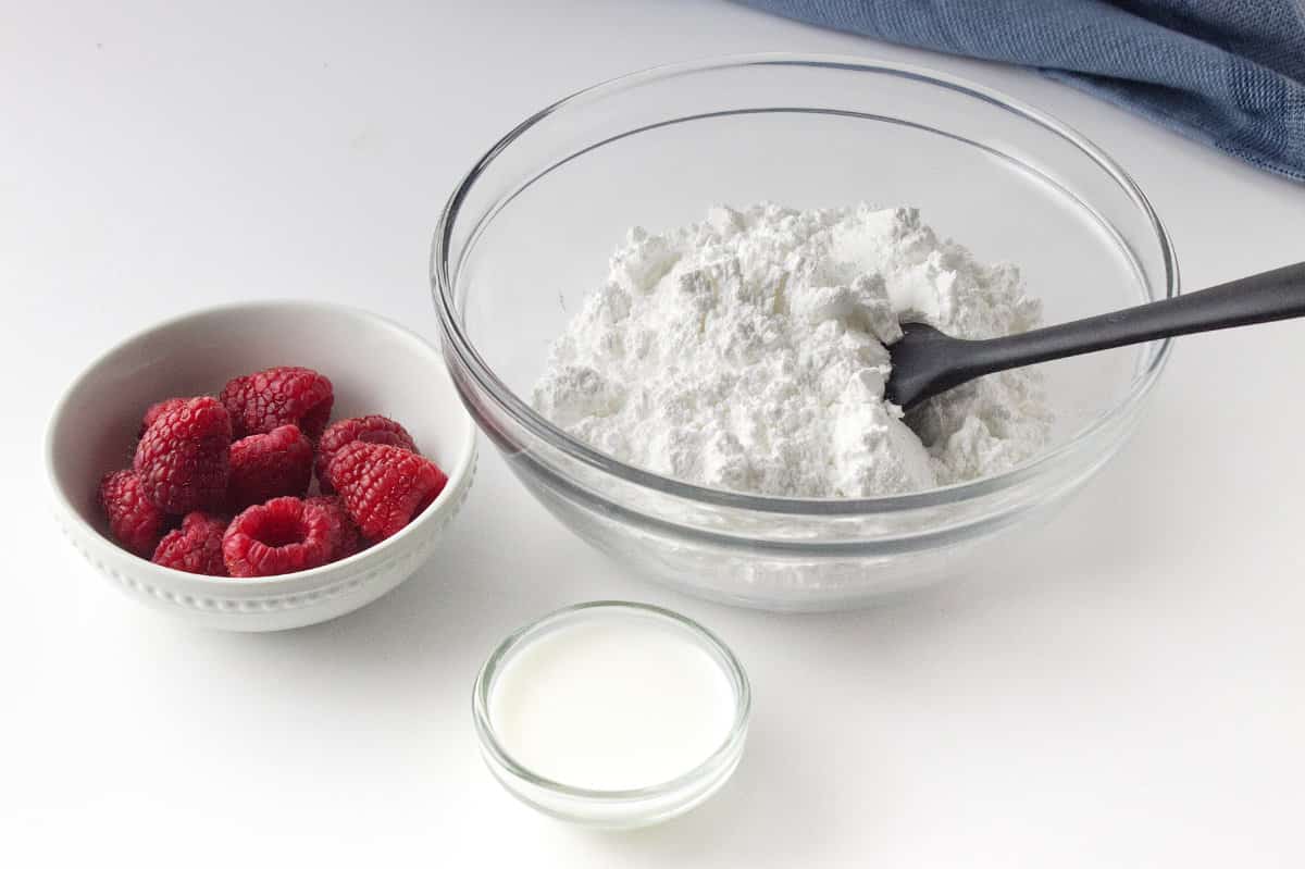 bowls of icing ingredients, powdered sugar, cream, and fresh raspberries.