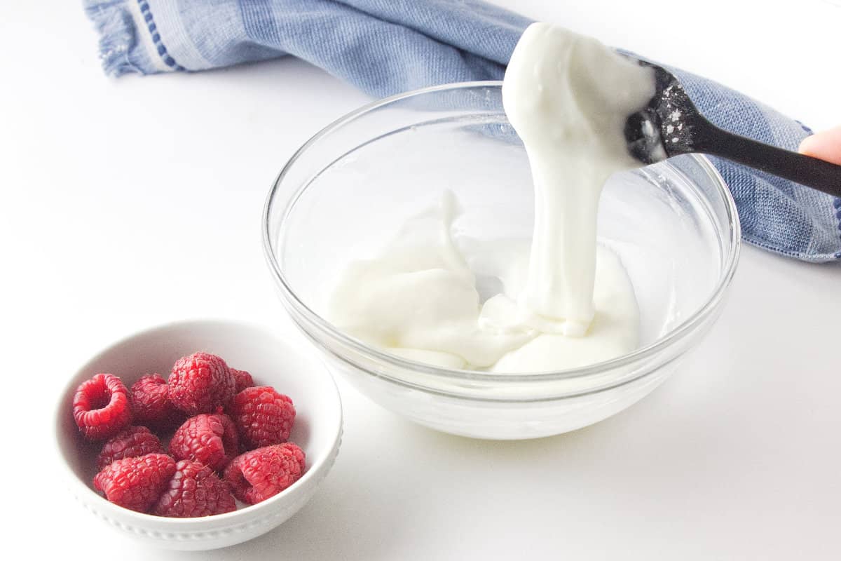 white icing in a bowl with a small bowl of fresh raspberries.