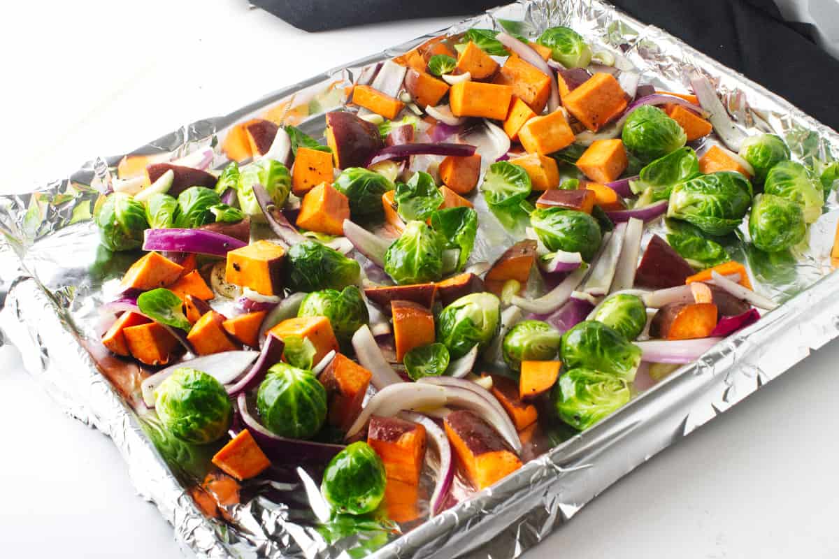 raw sweet potatoes and brussels sprouts on a cookie sheet.