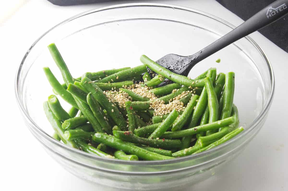 sesame seeds added to bowl of frozen green beans.