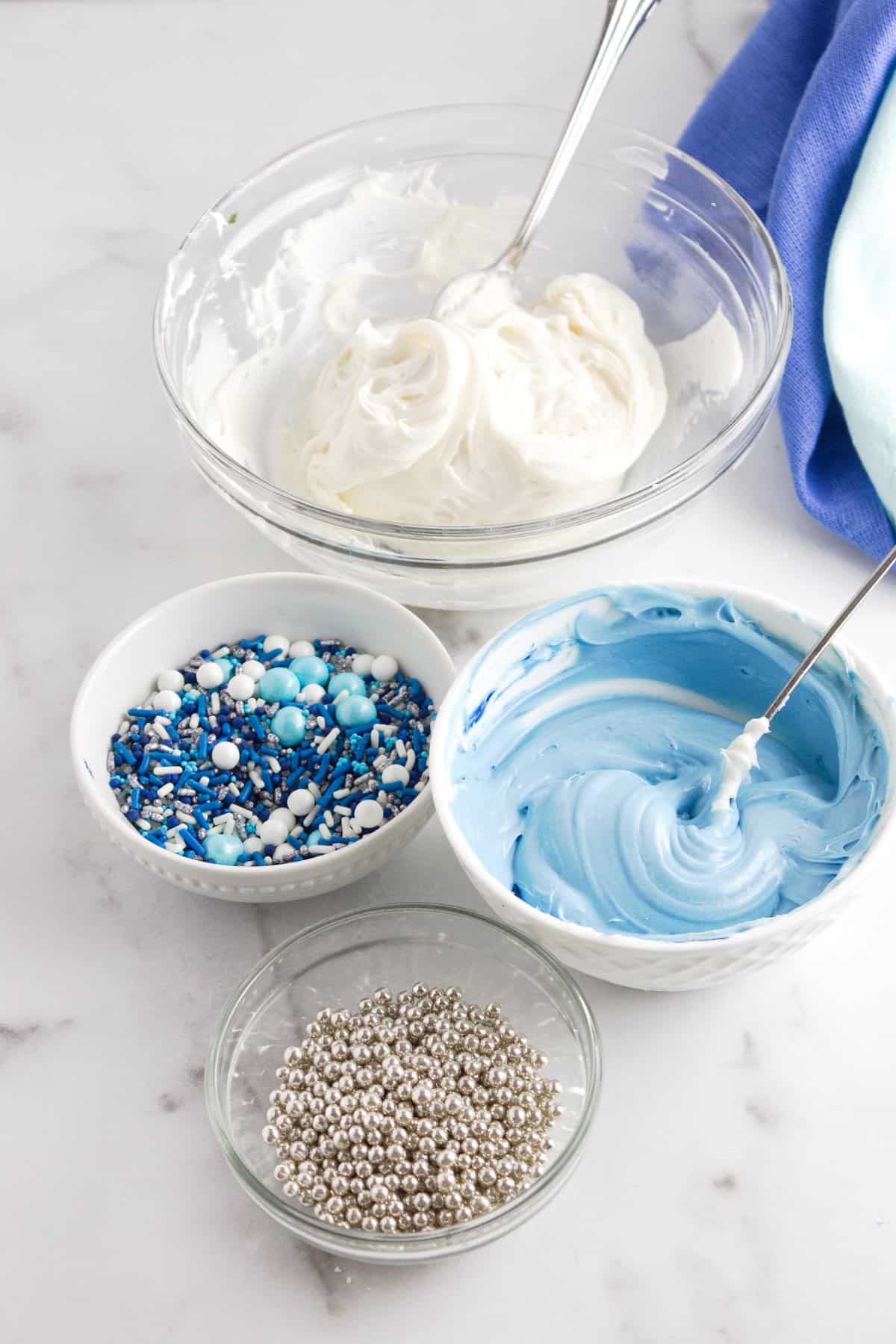bowls of white frosting, blue frosting, and Hanukkah sprinkle blend.