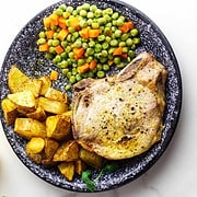seasoned pork chops with bone in, on a plate with peas and carrots and diced potatoes.