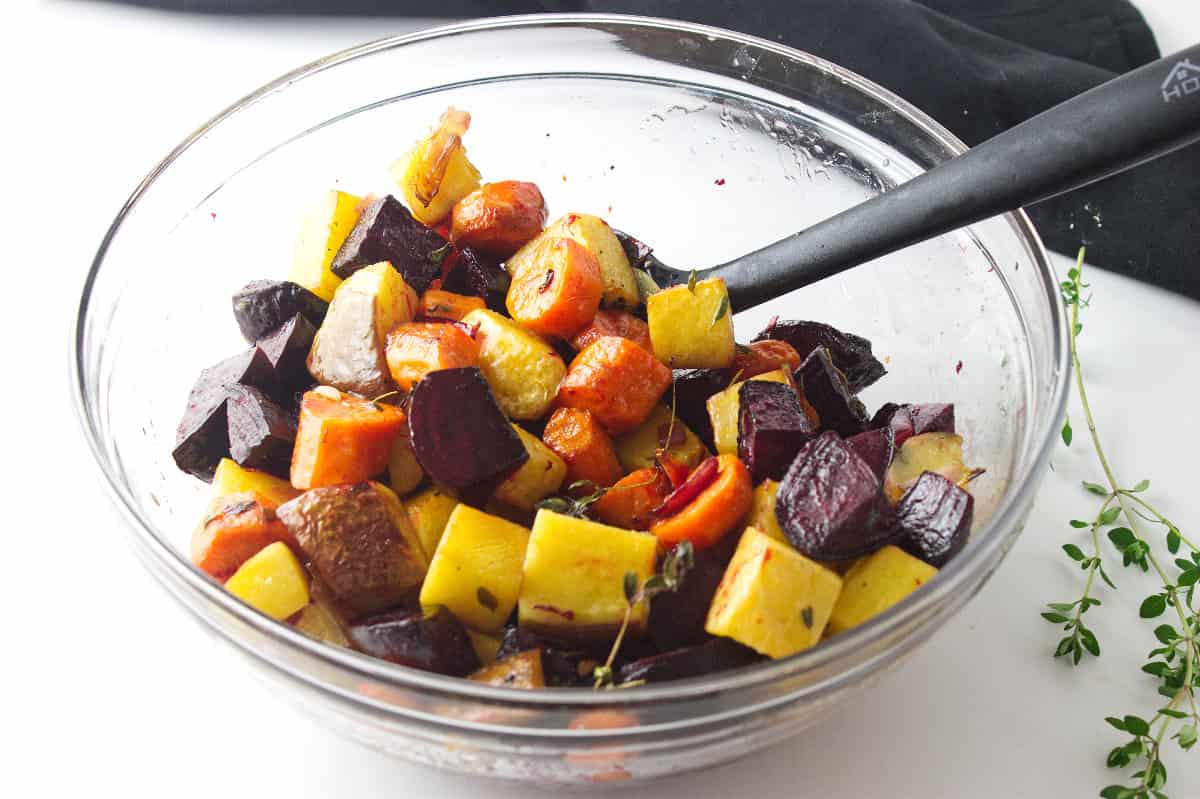 tossed cut carrots, beets, and rutabagas in a bowl with herbs and seasonings.