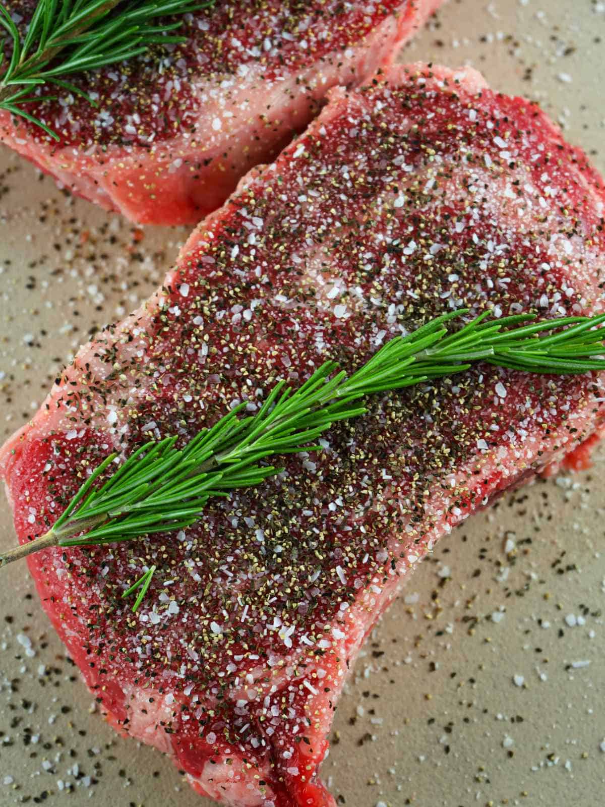steaks seasoned with coarse salt and sprigs of rosemary.