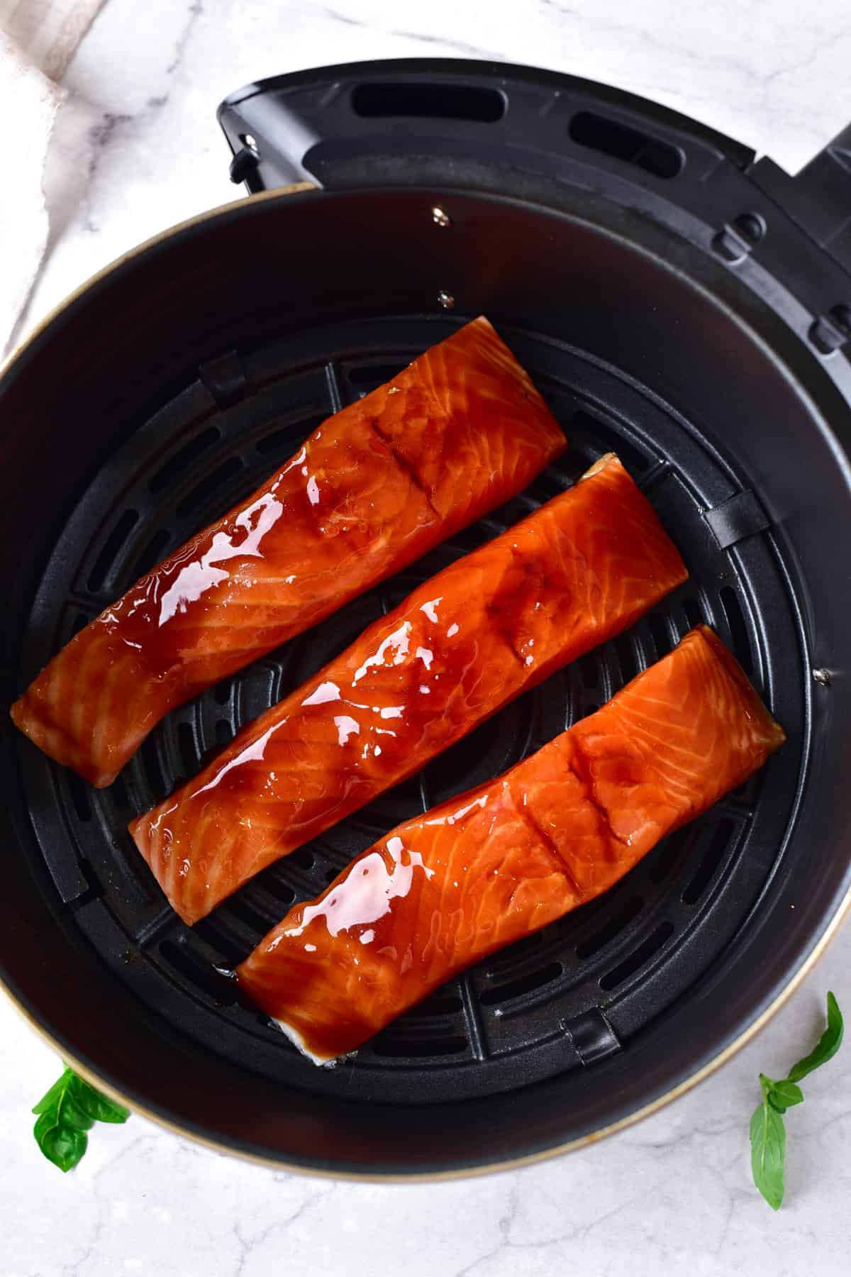 raw teriyaki glazed salmon steaks laid onto the basket bottom of an air fryer.