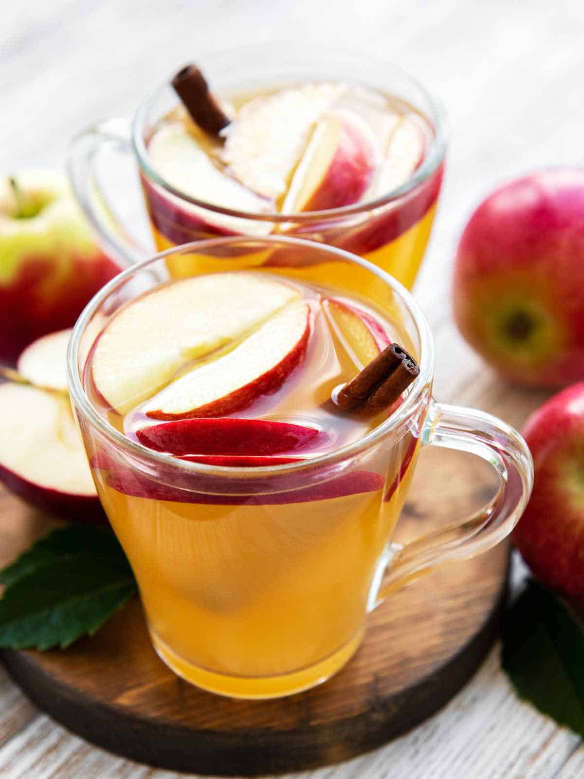 Apple cider beverage with apple slices and cinnamon sticks.
