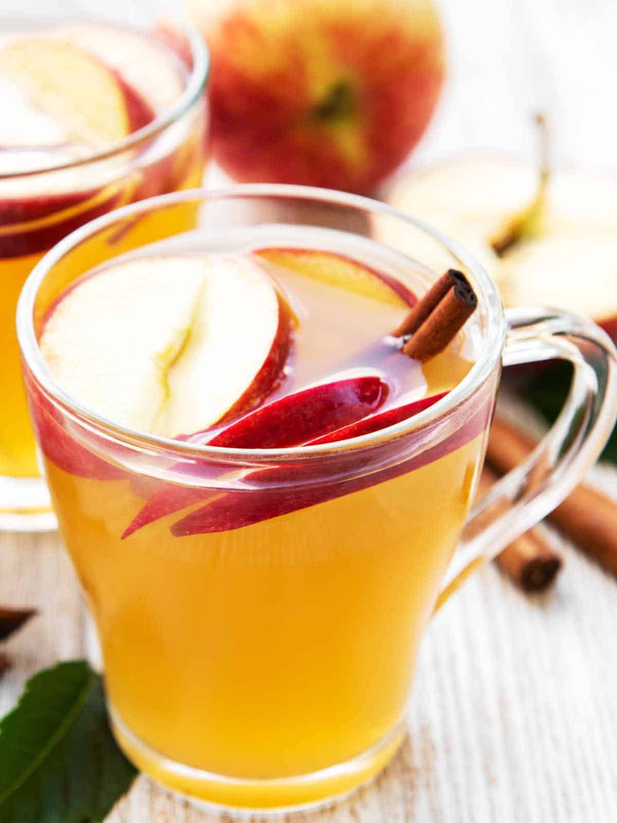 Apple juice in a glass with apple slices and cinnamon sticks.
