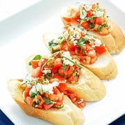 serving plate with four slices of french bread with a tomato and feta cheese topping.