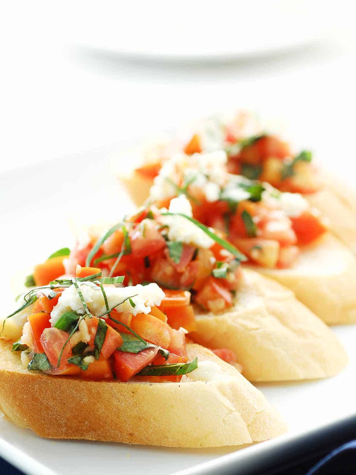 serving plate with four slices of french bread with a cherry tomato bruschetta.
