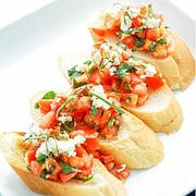 serving plate with four slices of french bread with a tomato and feta cheese topping.