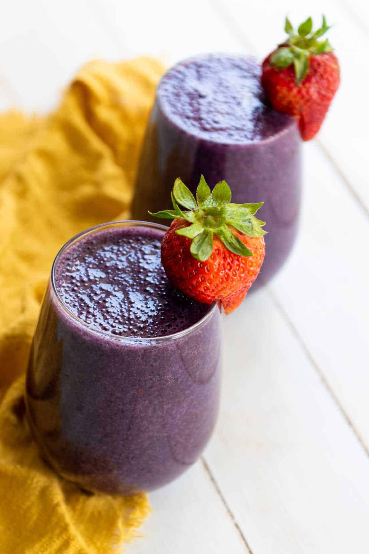 two stemless wine glasses filled with berry smoothie's, garnished with a strawberry on the rim.