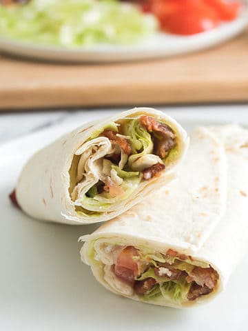 Bacon Lettuce and Tomato rolled up wrap on a plate and sliced in half.