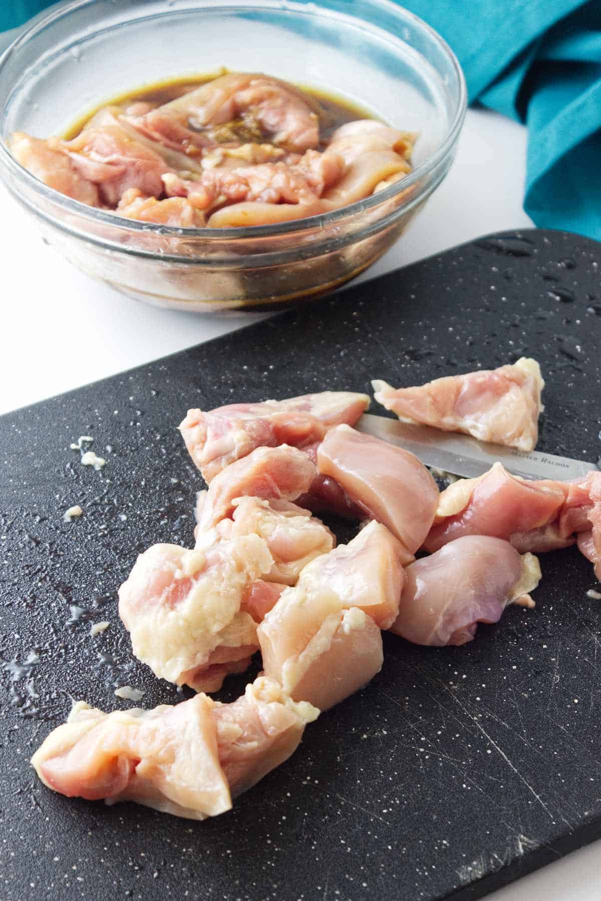 bowl of cut up chicken thighs in a bowl and on cutting board.