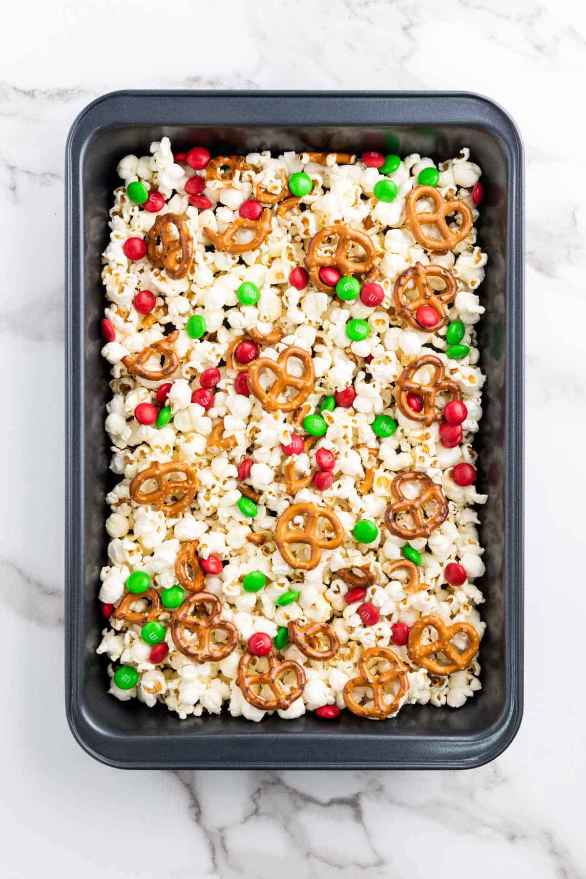 pretzel knots and holiday M&M's added snack mix in baking pan.