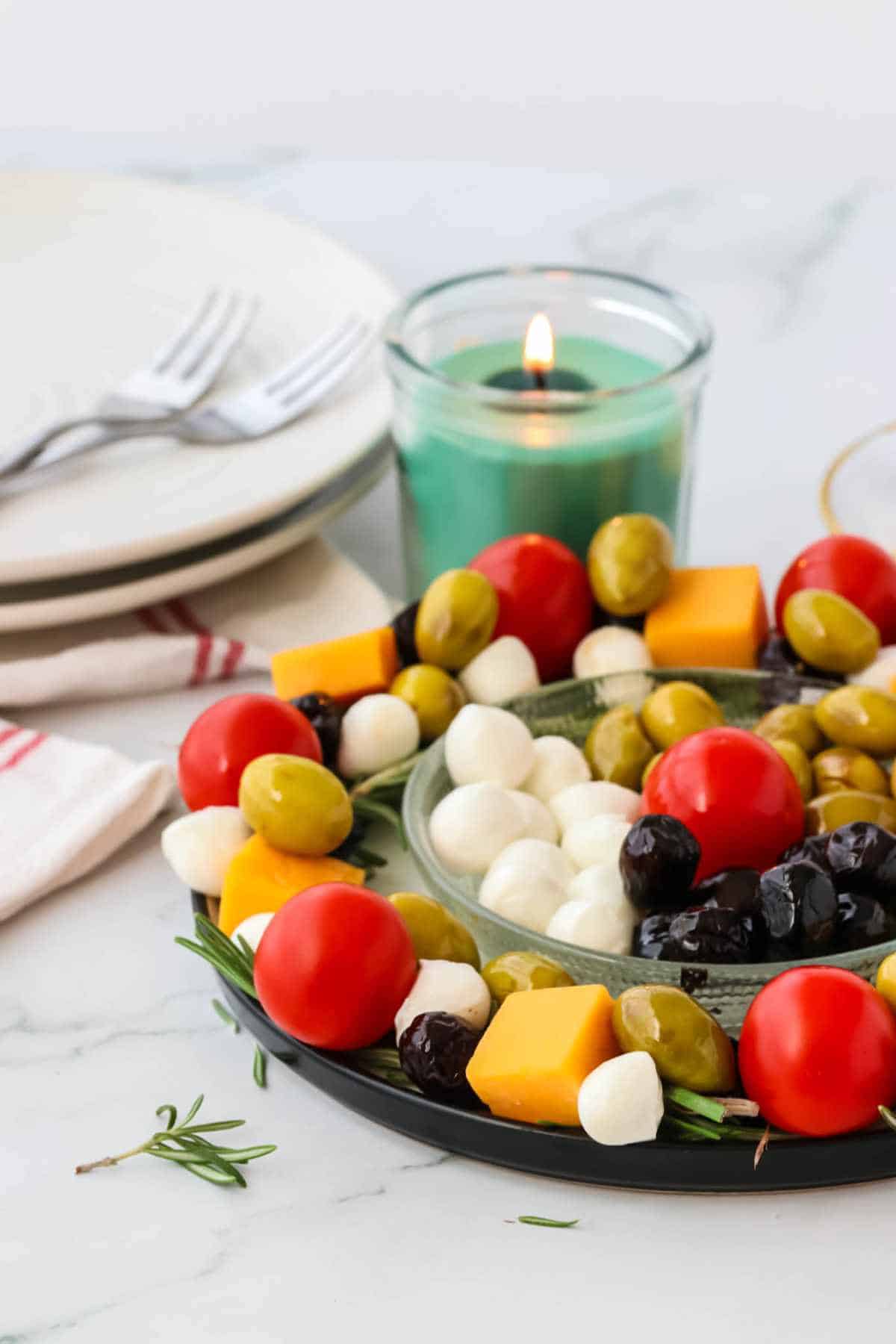 christmas wreath appetizer with center bowl of additional cheese, olives, and tomatoes.