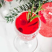 tall crystal flute filled with cranberry mimosa garnished with a rosemary sprig and cranberries.