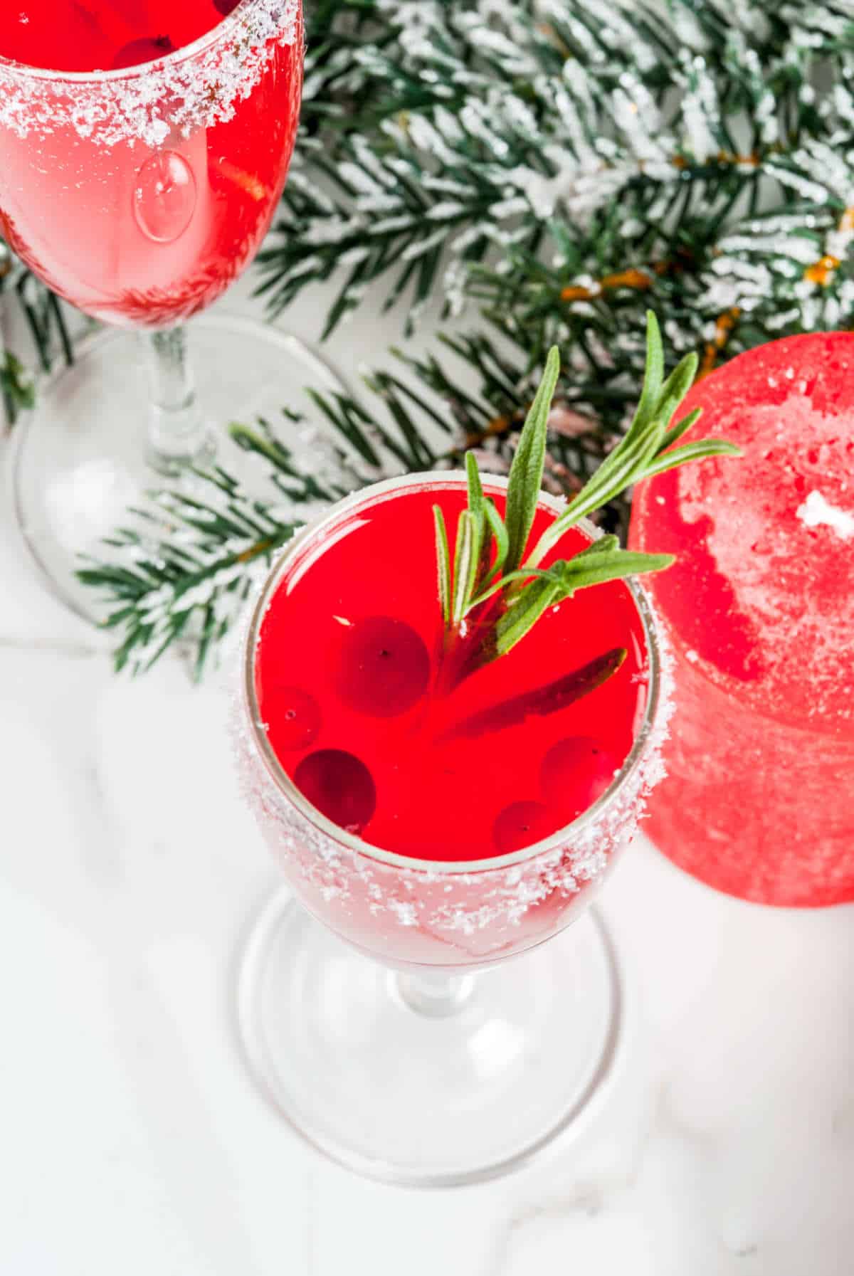 tall crystal flute filled with cranberry juice and sparkling wine, garnished with a rosemary sprig and cranberries.