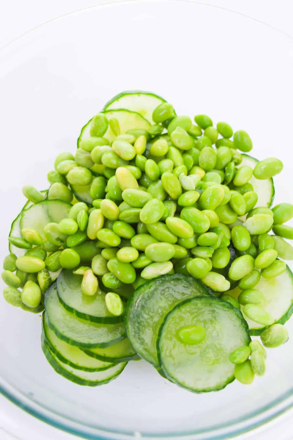 fresh or frozen edamame beans added to bowl with cucumber slices.