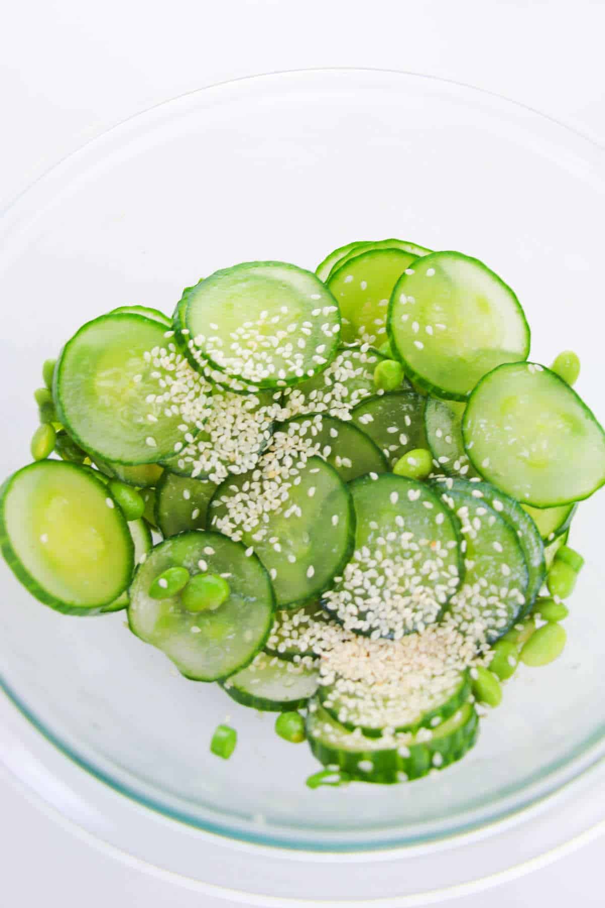 sesame seeds added to bowl of sliced cucumber and edamame beans.