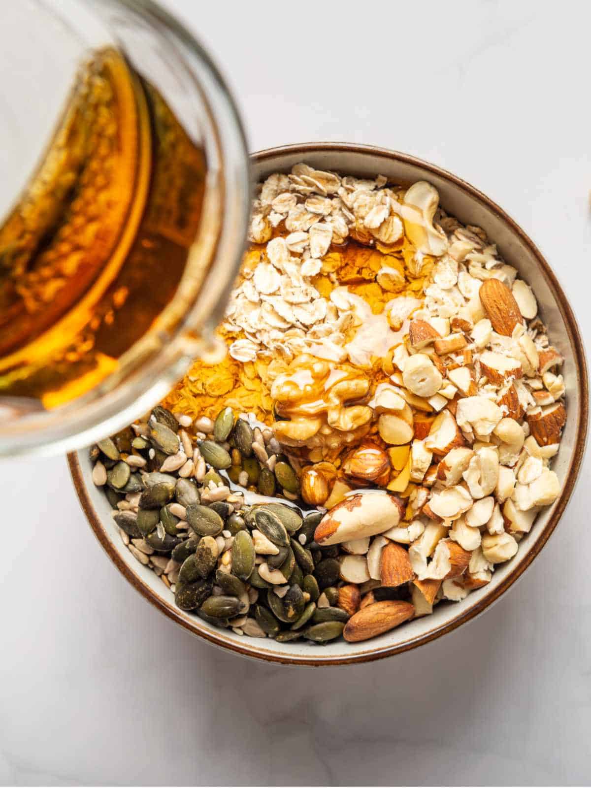 honey poured over a bowl of nuts, dried fruits, seeds, and rolled oats.