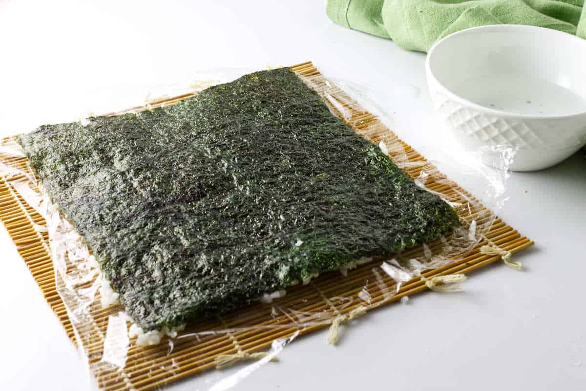 Rice covered seaweed sheet flipped over for making inside out korean kimbap roll.