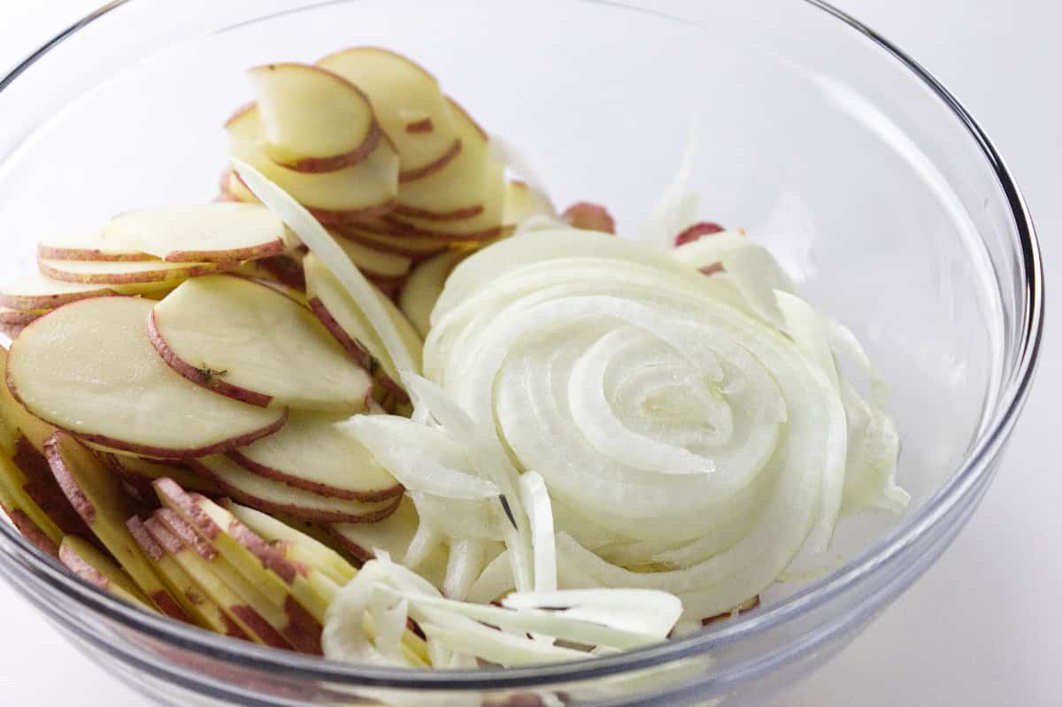 clear glass bowl of thinly sliced red potatoes and onion.