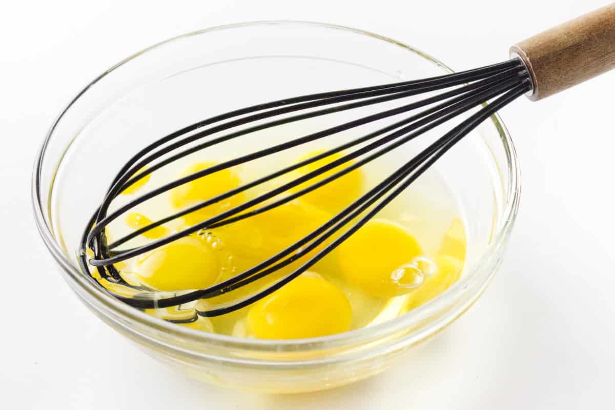 clear glass bowl with six eggs. with whisk ready to blend or beat them.