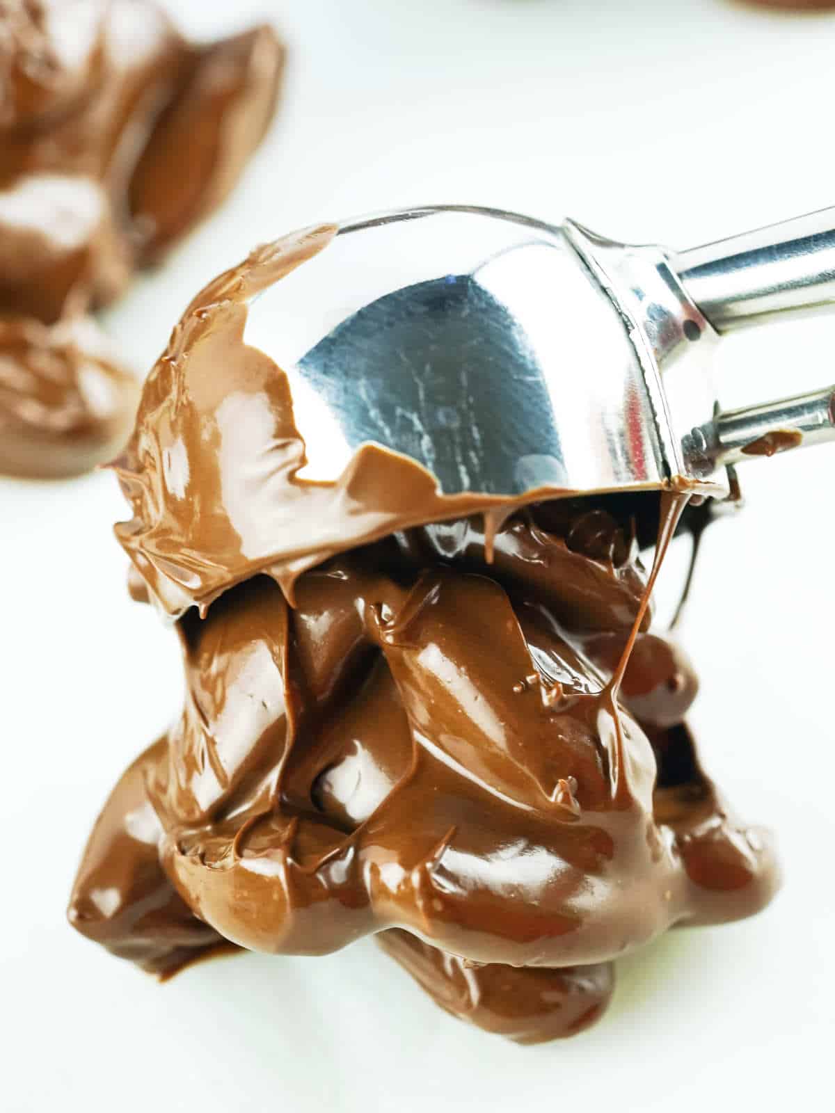 Scoop of melted chocolate covered almonds being placed on parchment paper.