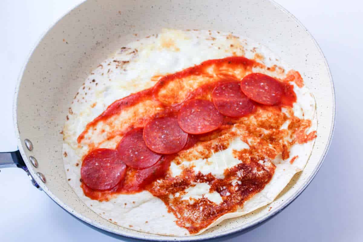 slices of pepperoni on top of pizza sauce, browned cheese, and flour tortilla.