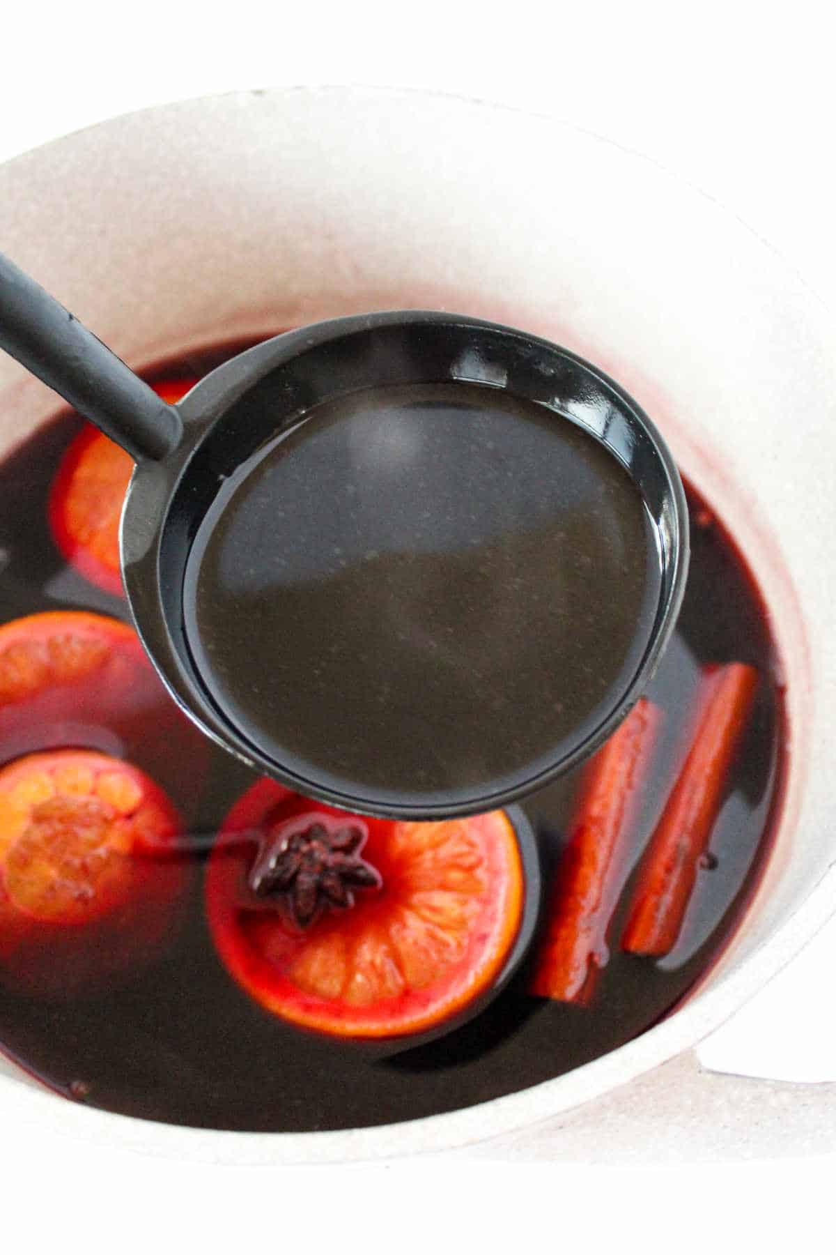 Pot of mulled wine with slices of orange, cinnamon sticks, and star anise.