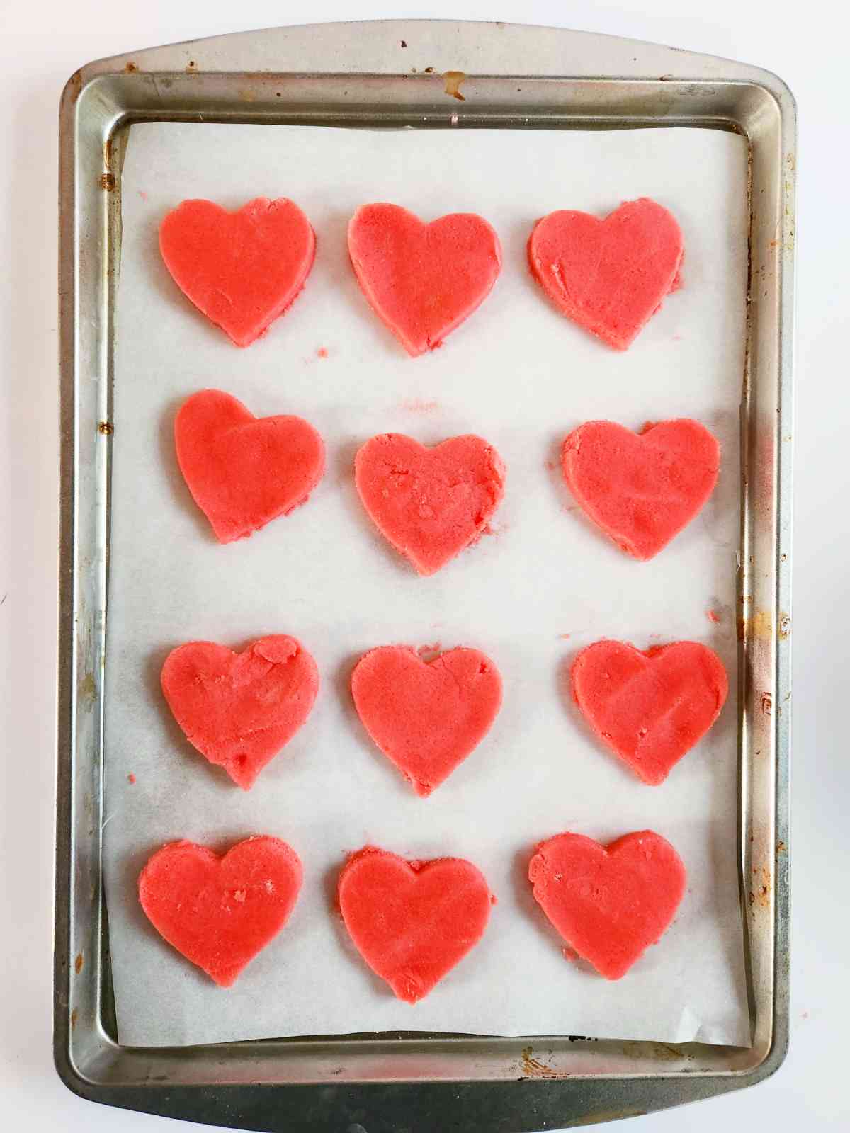 heart shaped pink sugar cookies on a baking sheet ready to bake.