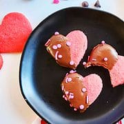 sprinkles on chocolate dipped pink heart cookies black plate.