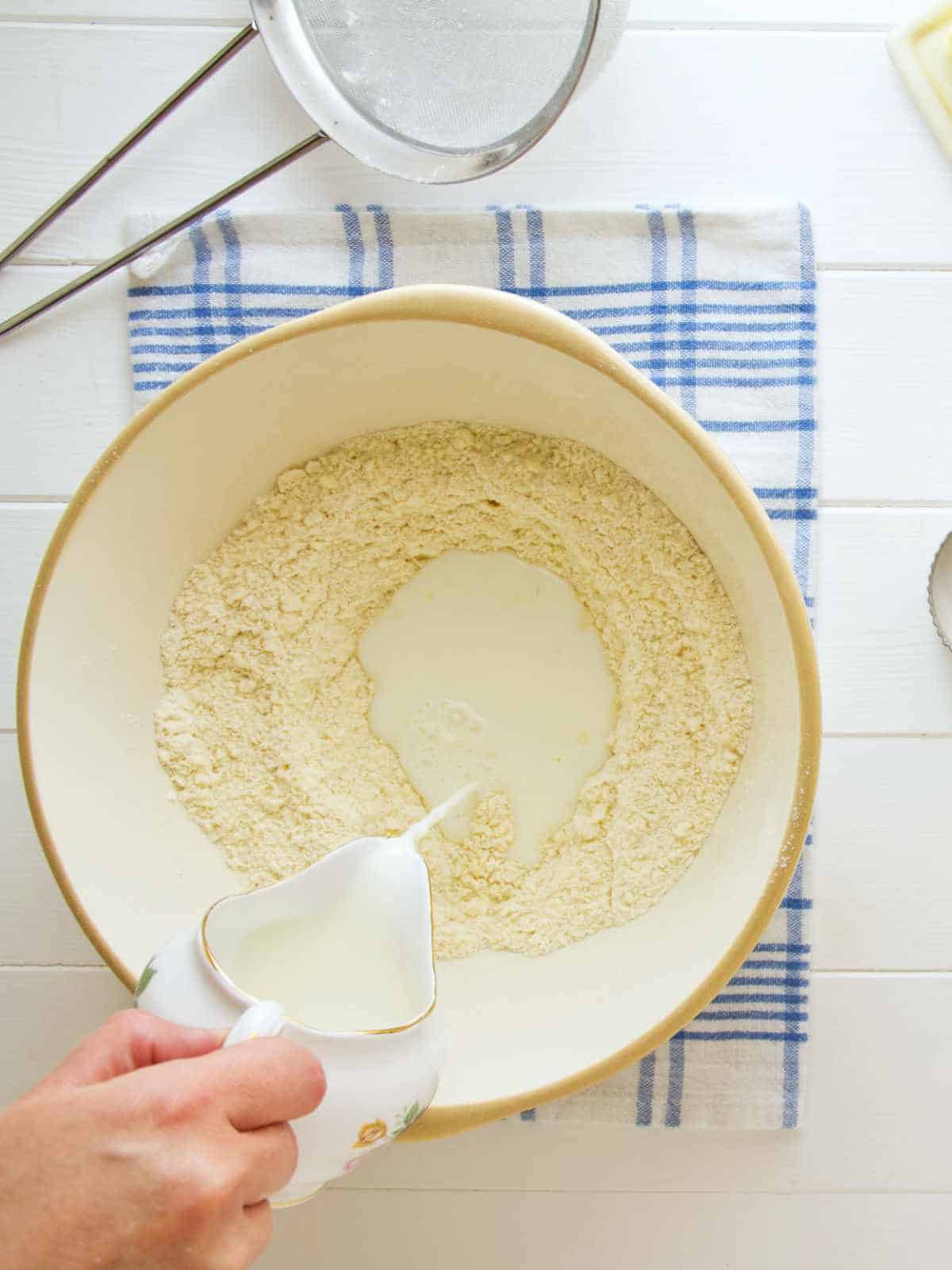 milk being added to bowl of flour.