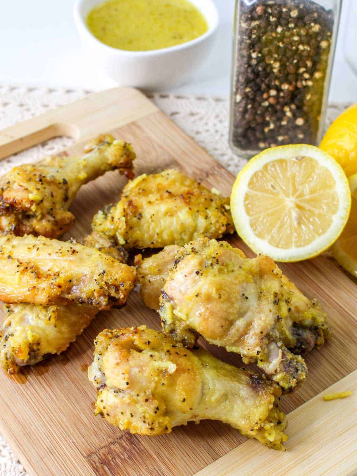 cutting board with honey lemon pepper chicken wings and half a lemon.