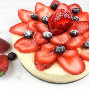 Cheesecake with sliced strawberries garnish with some blueberries and powdered sugar.