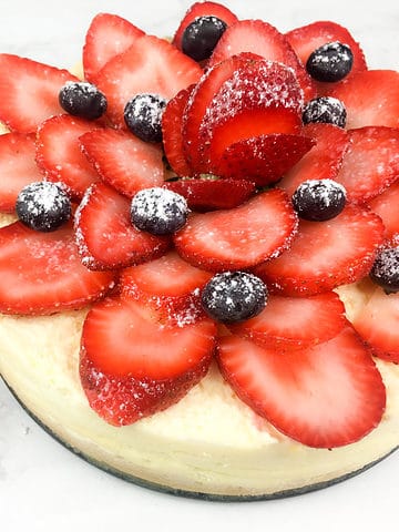 Cheesecake with sliced strawberries garnish with some blueberries and powdered sugar.