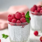 two glasses of chia pudding topped with fresh raspberries.