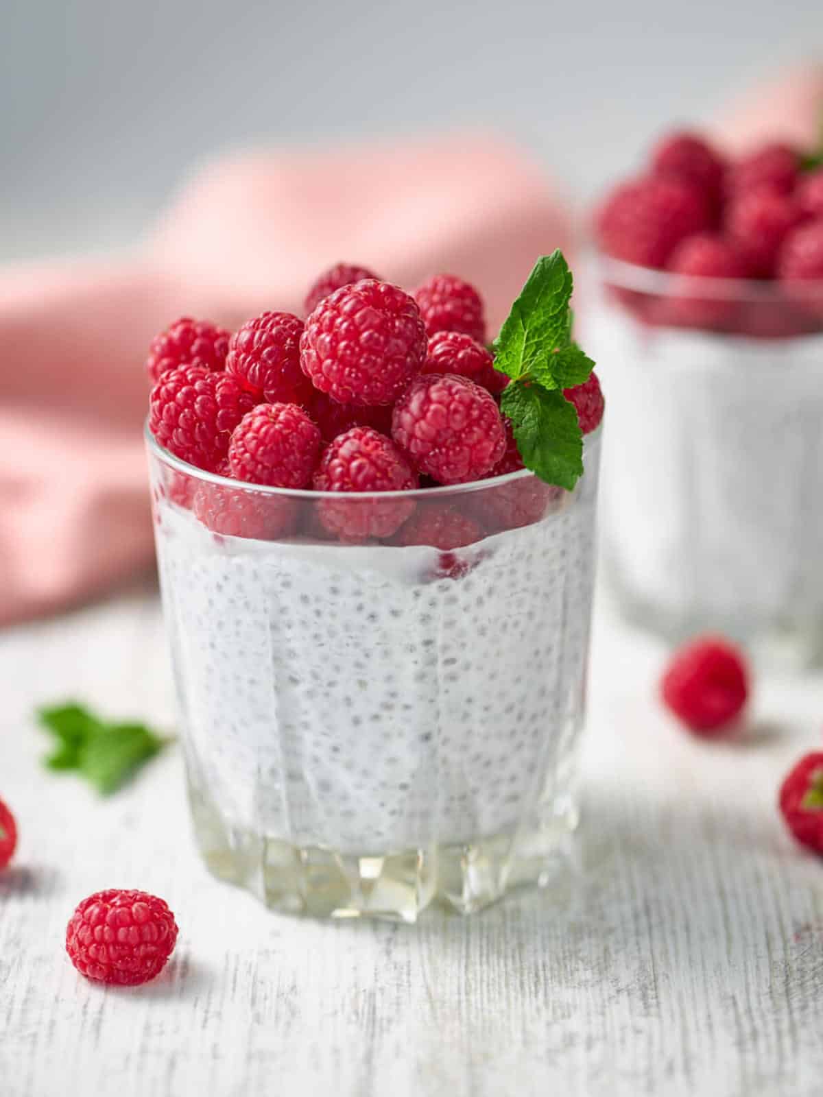 two glasses of chia seed pudding topped with fresh raspberries.