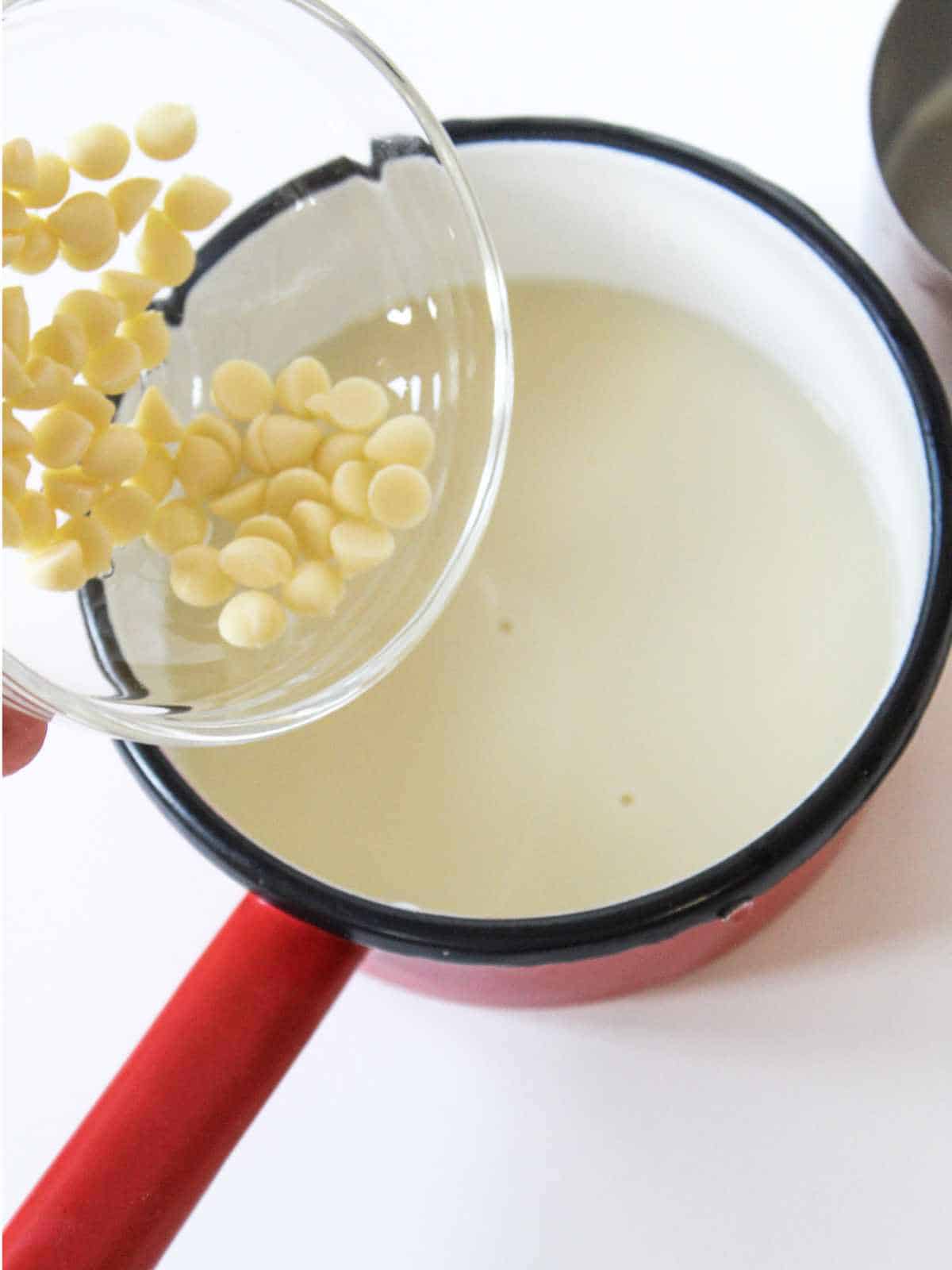 Adding white chocolate chips to a saucepan of milk.