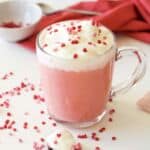 Whip cream and sprinkles on top of a mug of pink hot chocolate.