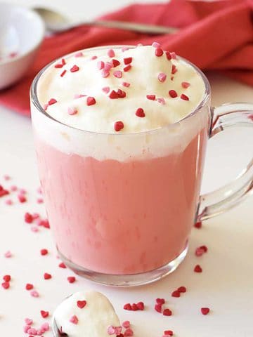 Whip cream and sprinkles on top of a mug of pink hot chocolate.