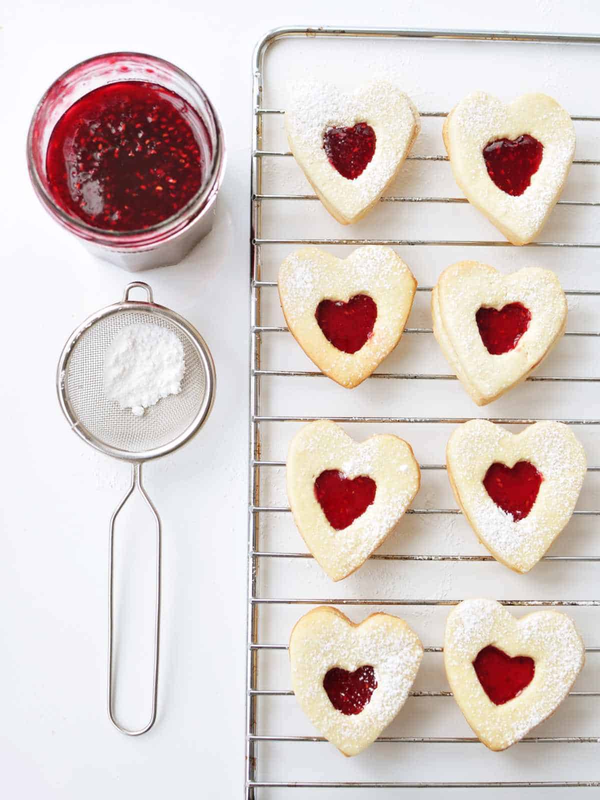 Heart shaped cookies put together as sandwich cookies. Sugar dusted top cutouts placed on hearts with raspberry jam on them.