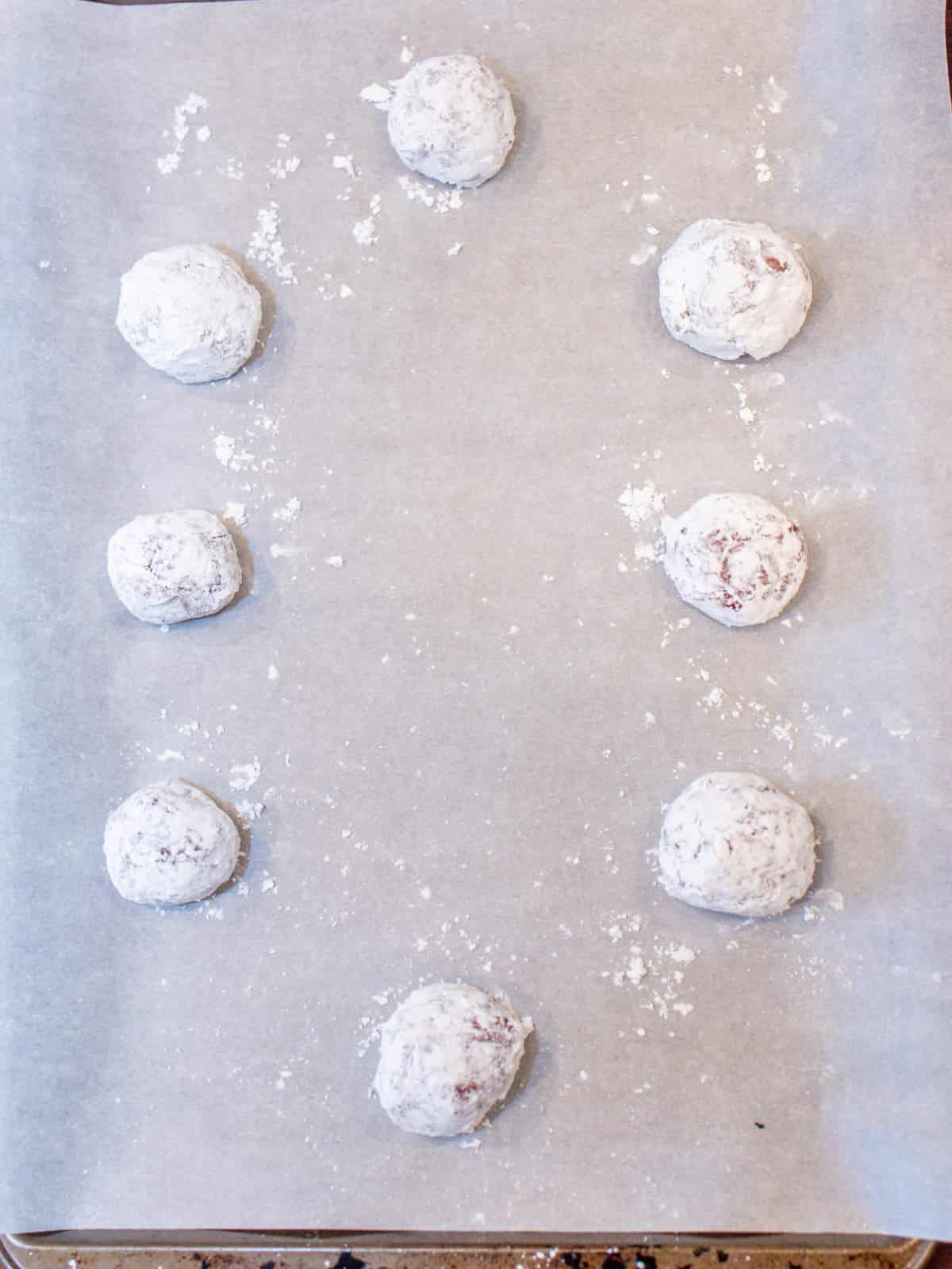 unbaked powdered sugar covered cookie balls on parchment paper covered baking sheet.
