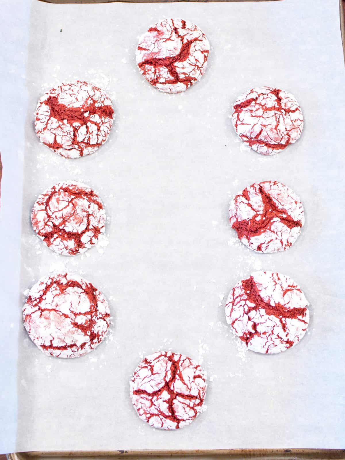 Baked red velvet cookie crinkle cookies on parchment paper covered baking sheet.
