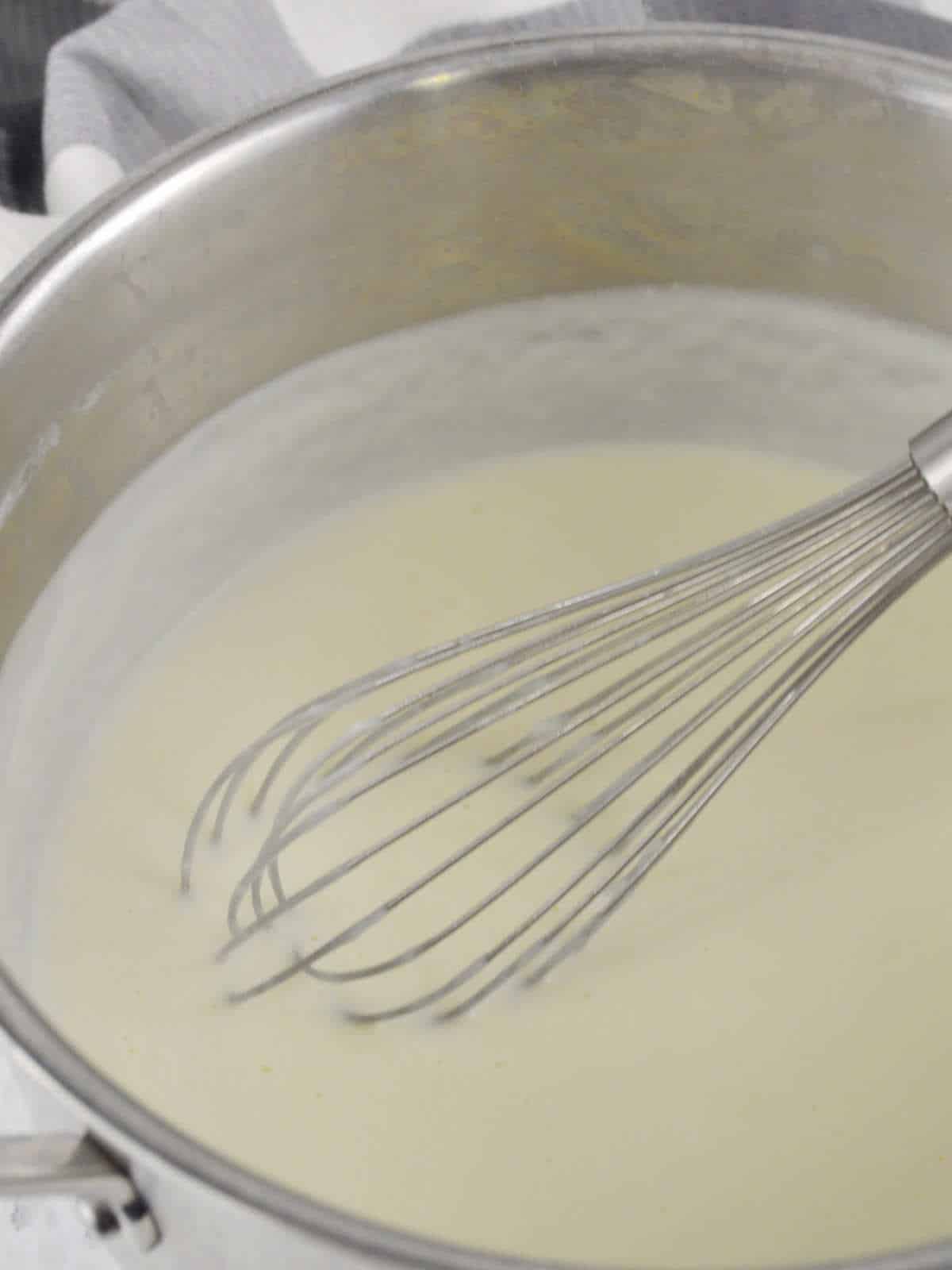 saucepan and whisk with Alfredo sauce cooking for seafood lasagna recipe.