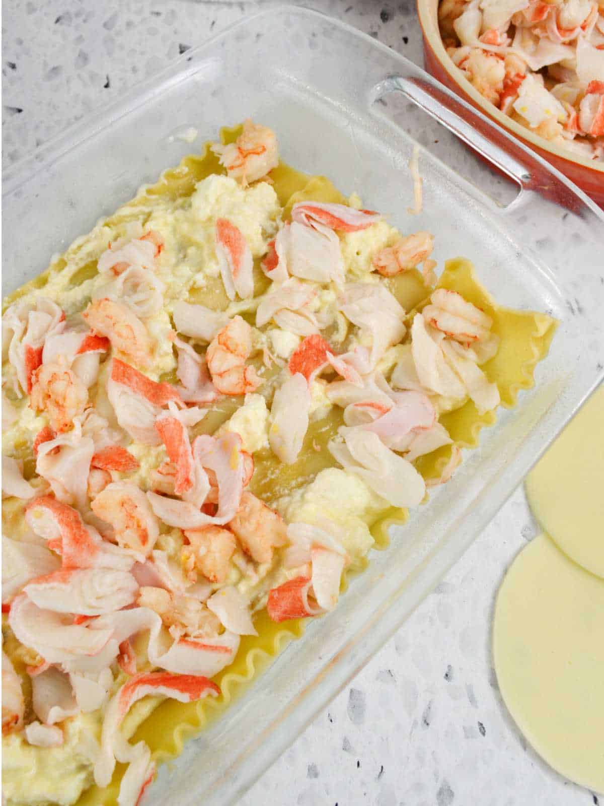 layers of pasta ribbon, bechamel sauce, crab, and shrimp in a casserole dish.