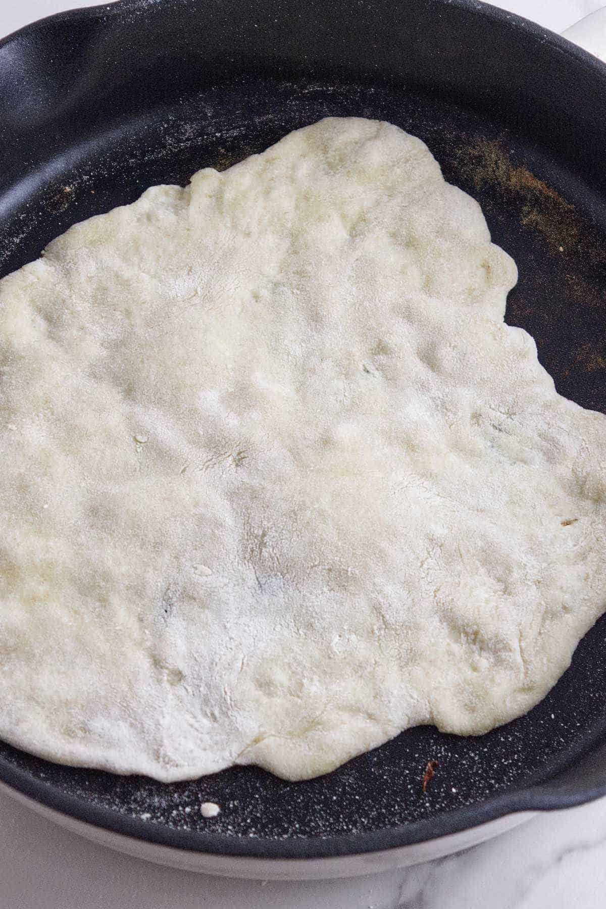 dough being cooked on one side in a hot skillet.