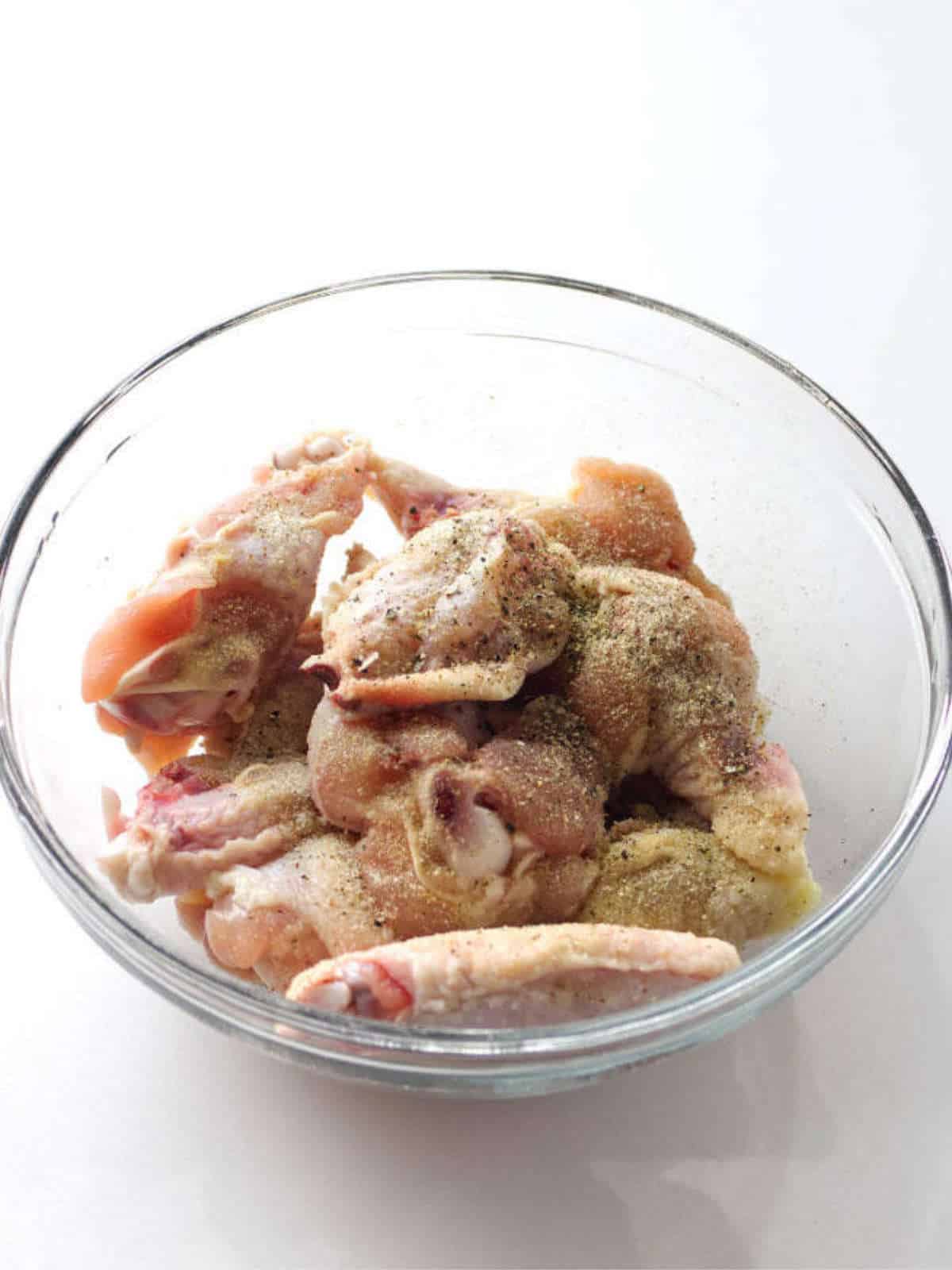 chicken wings in a bowl with seasonings.