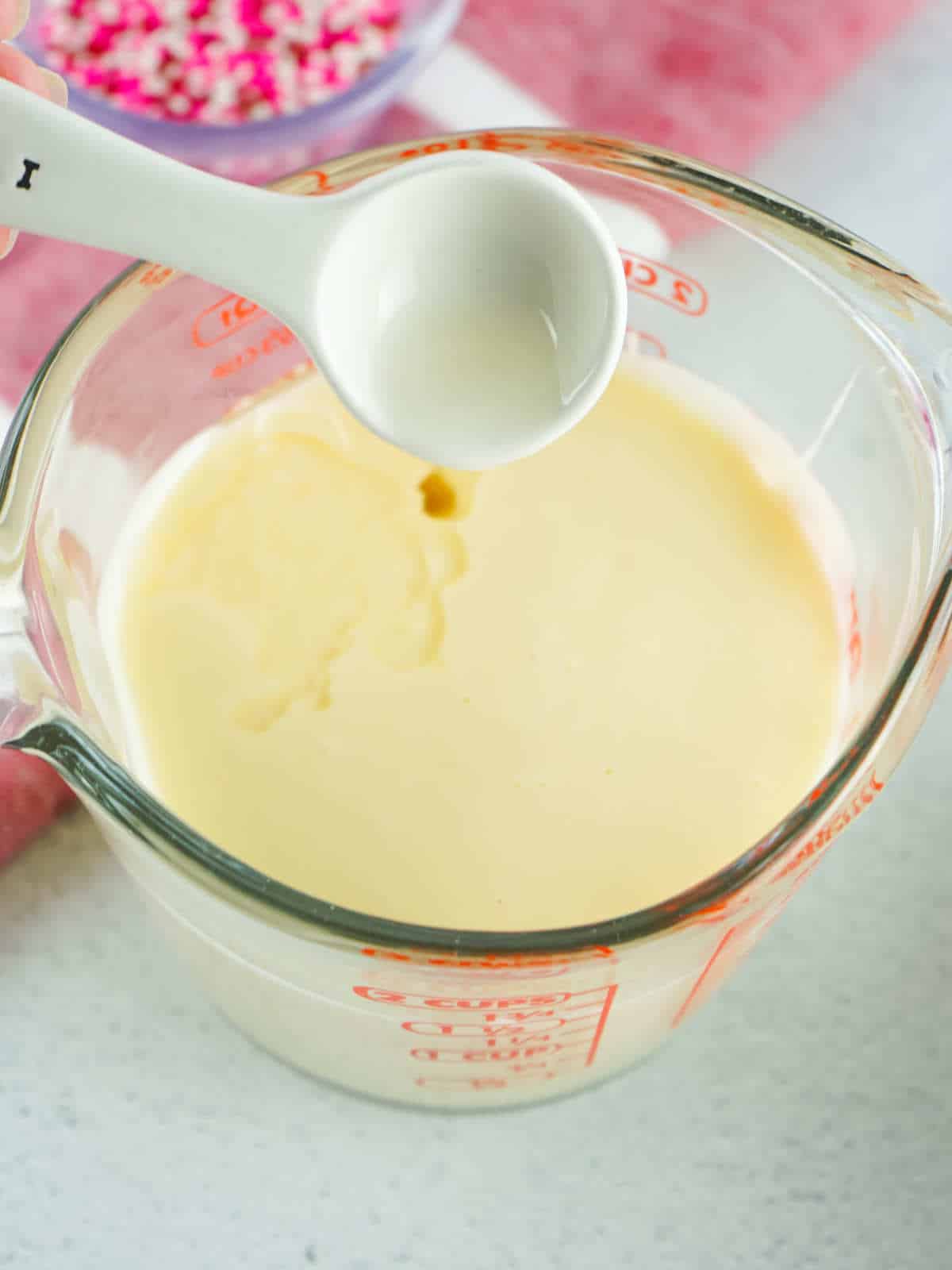 Melted buttercream frosting in a Pyrex measuring cup with vanilla being added.